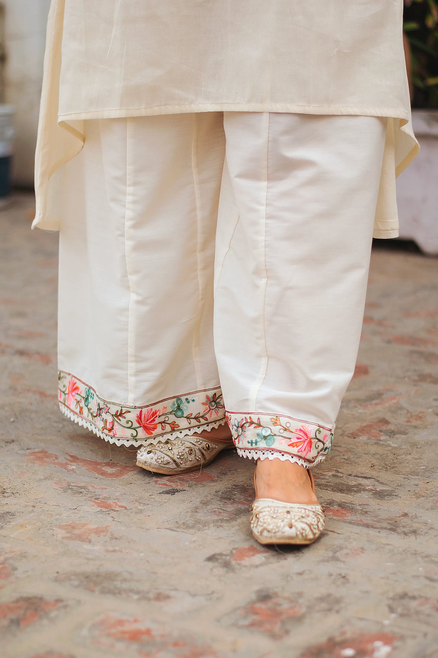 An Indian woman wearing an off-white asymmetric kurta set, showcasing the matching palazzo pants and footwear