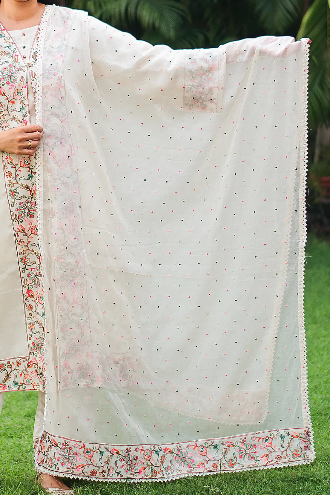 Indian model holding an off-white cotton dupatta with multicolored Kashmiri floral embroidery and lace detailing.