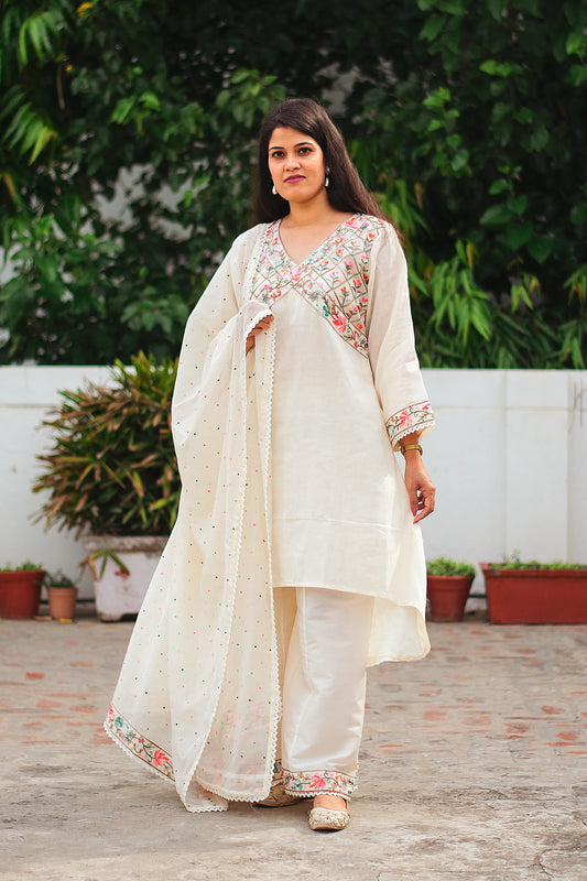 An Indian woman standing confidently in a full-length view, wearing a beautifully detailed, off-white asymmetric kurta with matching palazzo pants and a flowing dupatta