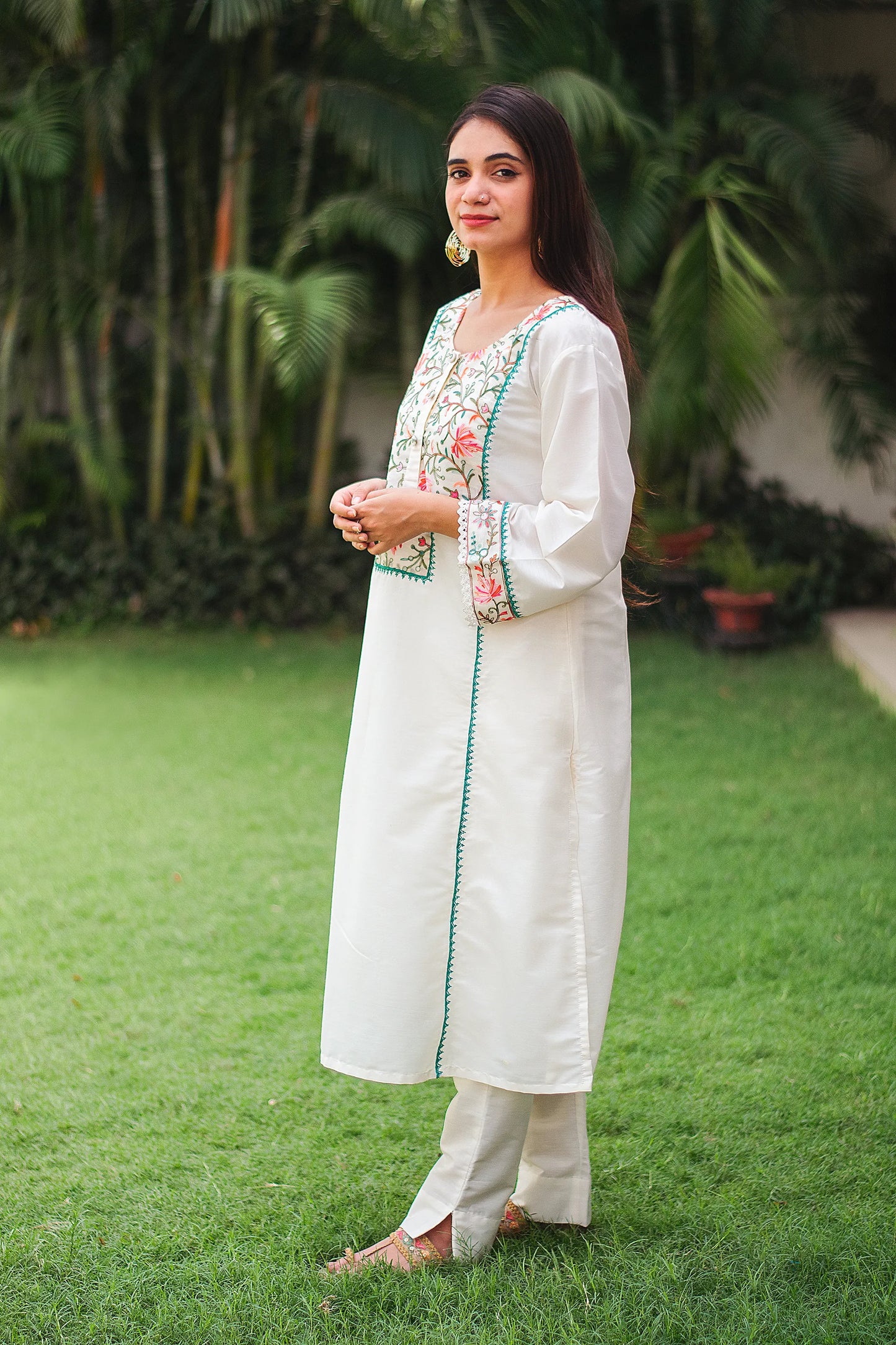 Side view of an Indian model in an off-white cotton kurta with Kashmiri embroidery and off-white trousers