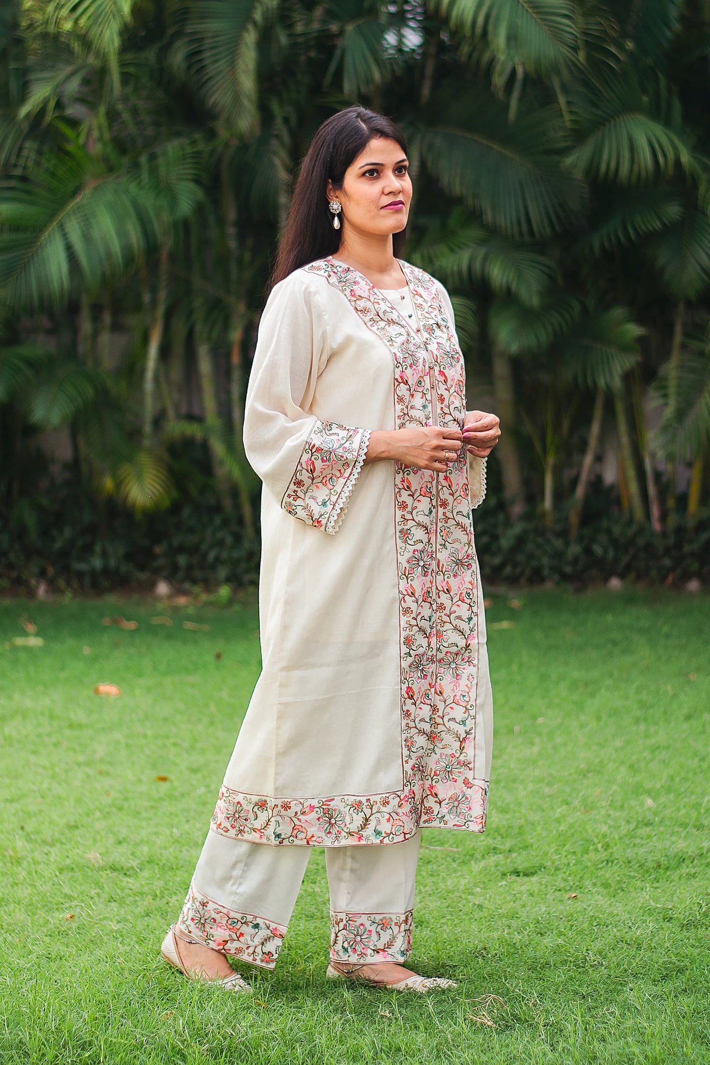 Side view of Indian model in an off-white cotton kurta with Kashmiri embroidery and off-white trousers.