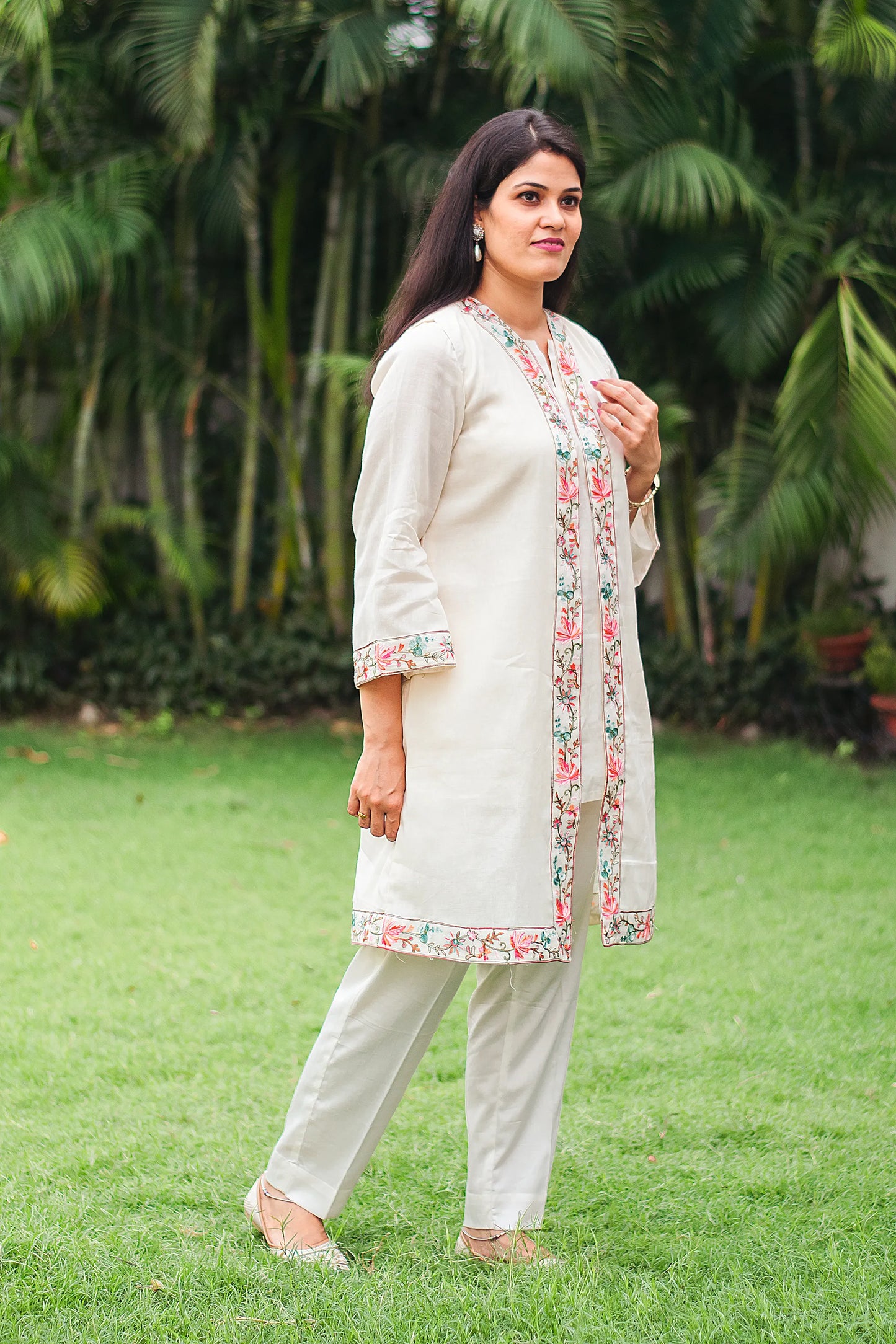 Indian model posing in profile, showcasing a beautiful off-white tunic and trousers set with delicate Kashmiri embroidery, paired with a matching dupatta