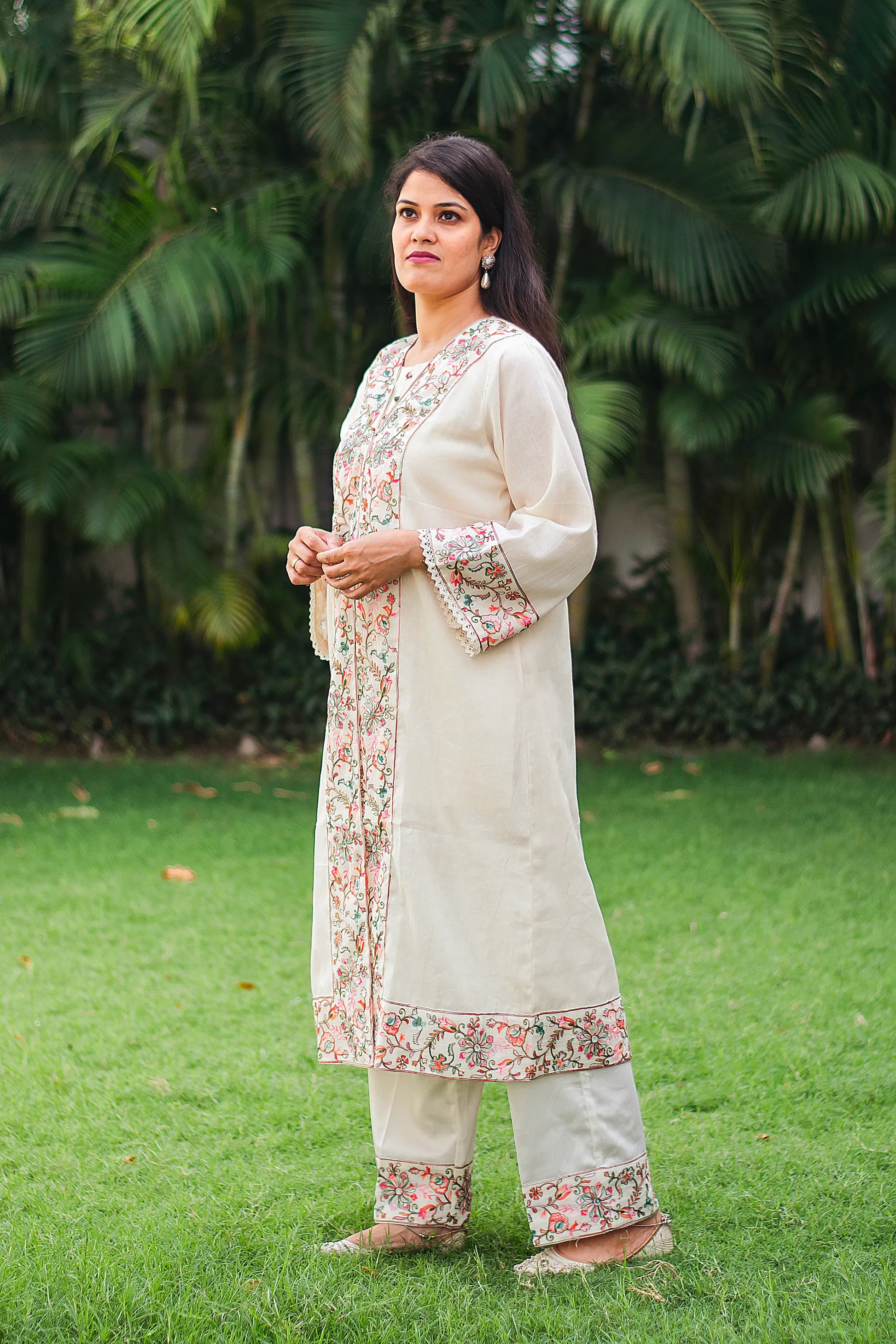 Side profile of Indian model wearing an off-white front open kurta with Kashmiri embroidery and matching trousers.