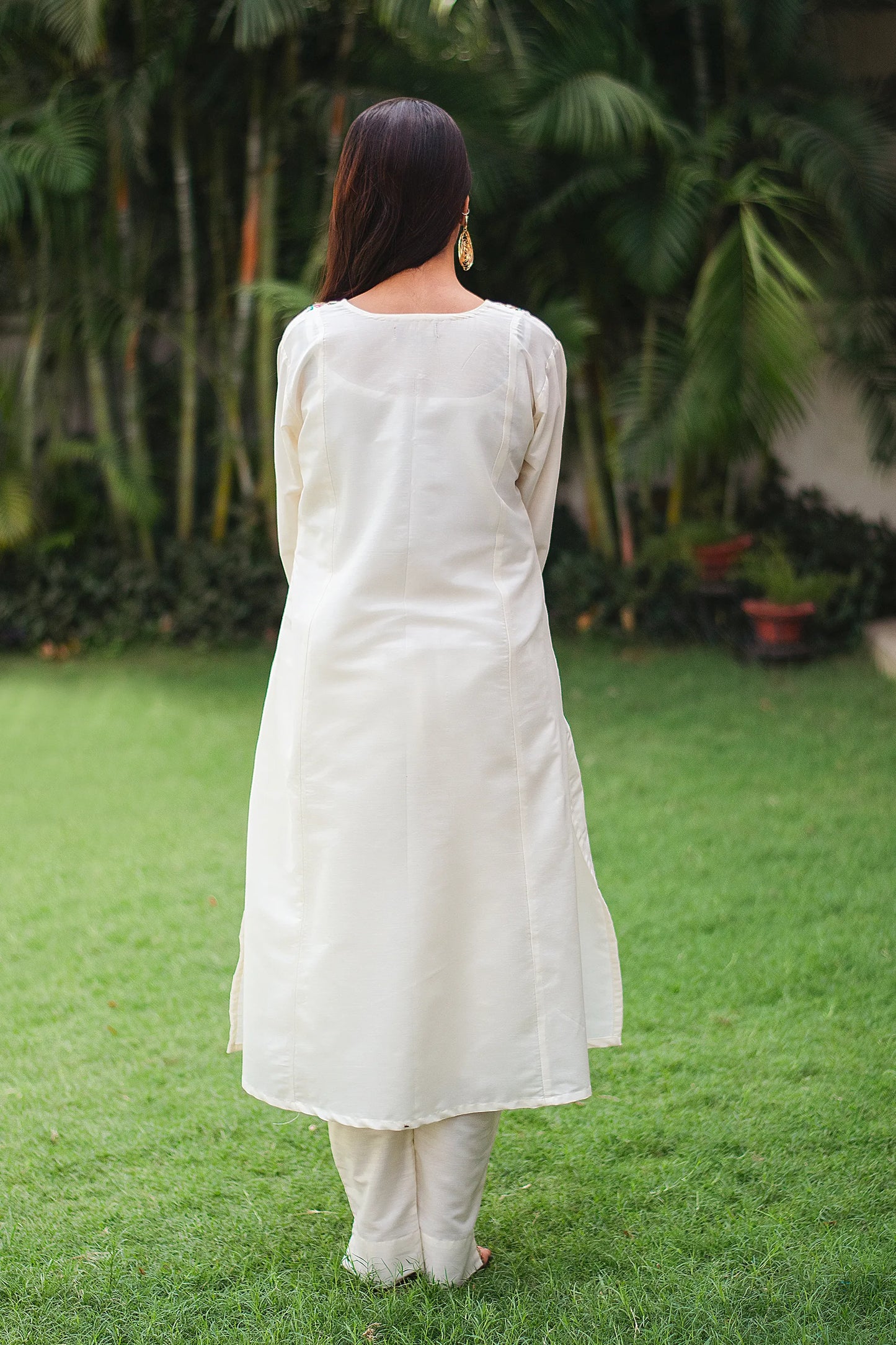 Back view of an Indian model wearing an off-white cotton kurta with Kashmiri embroidery and off-white trousers.