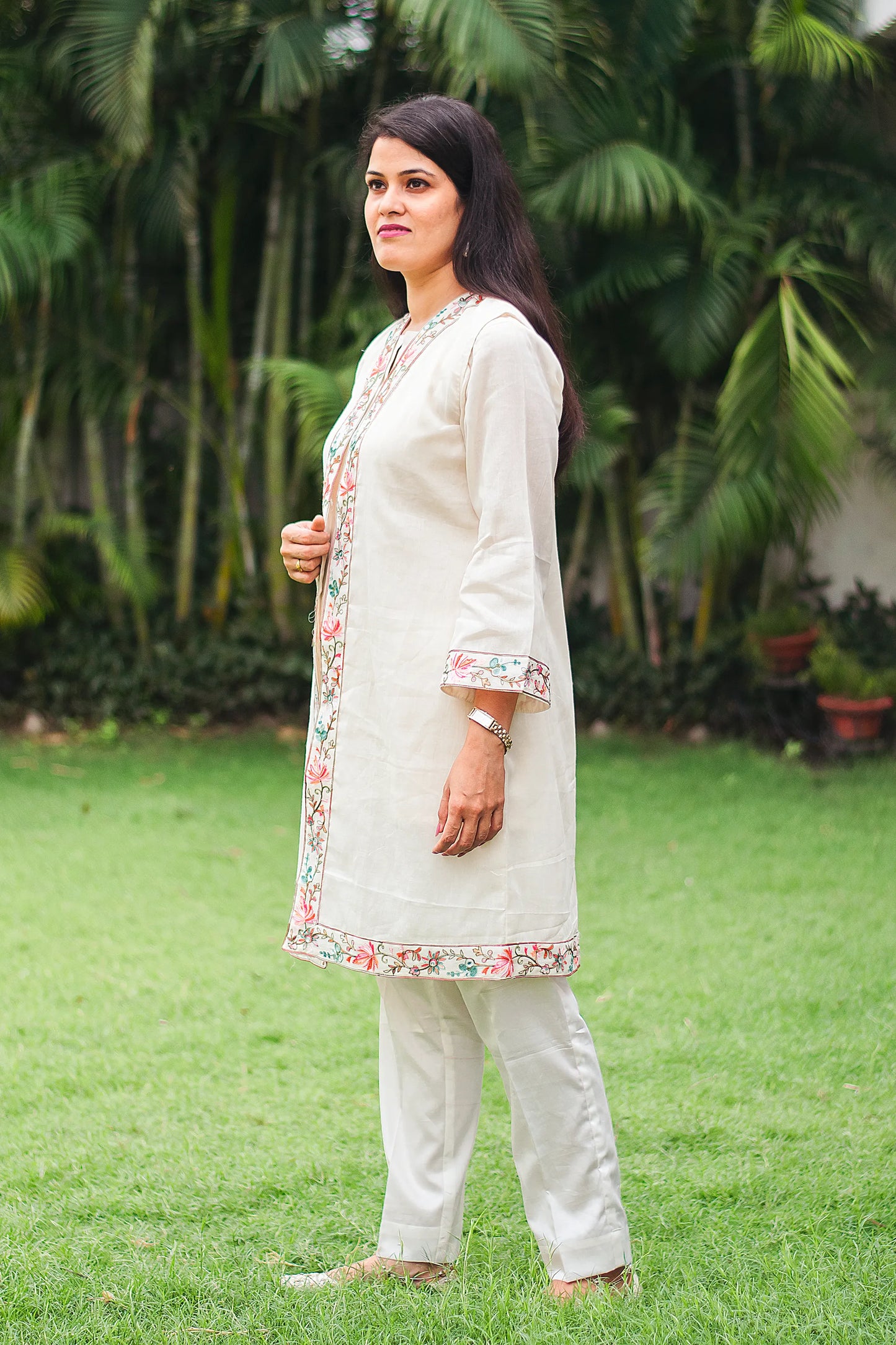 Indian model stands at a side angle, wearing an elegant off-white tunic and trousers set featuring intricate Kashmiri embroidery, complemented by a matching dupatta