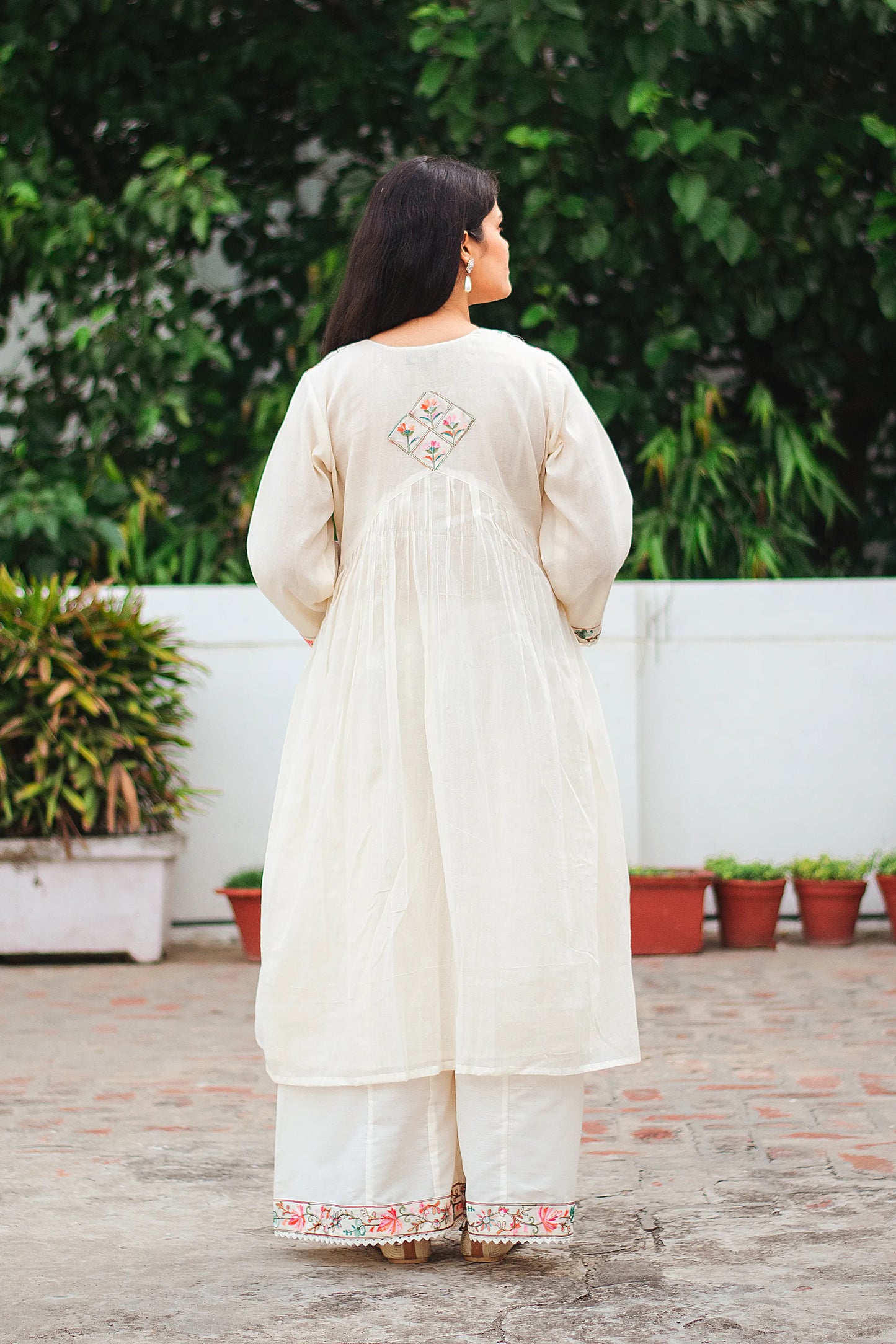 Back view of Indian model in an off-white cotton Anarkali kurta with floral embroidered motif at the back.