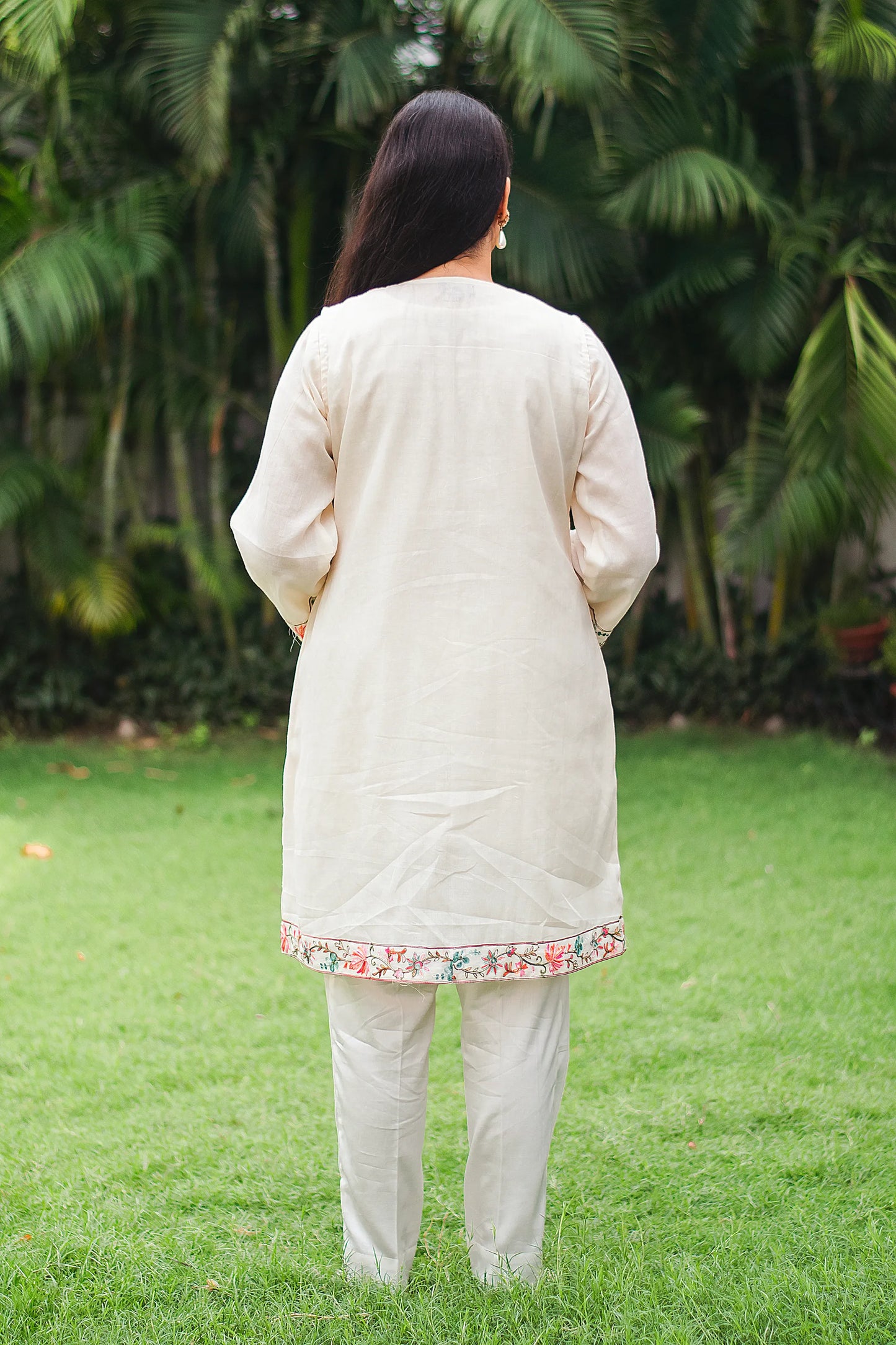 Indian model, back turned, wearing an elegant off-white tunic and trousers set featuring intricate Kashmiri embroidery