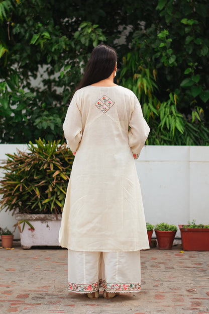 An Indian woman, her back to the camera showcasing an off-white asymmetric kurta, paired with matching palazzo pants