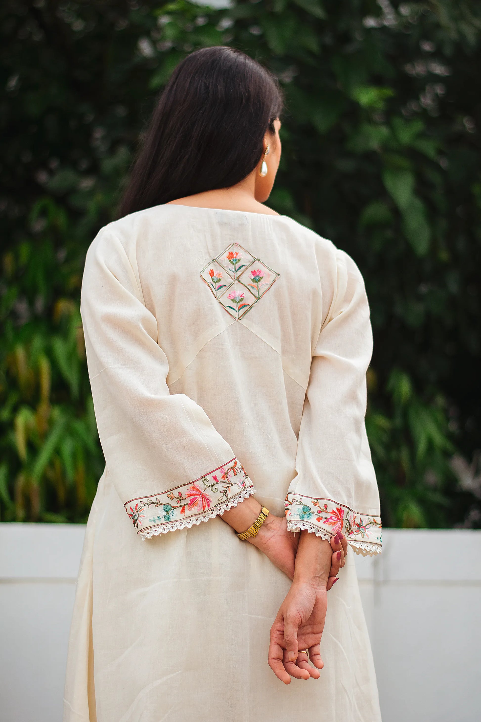 An Indian woman facing away, wearing an off-white asymmetric kurta set