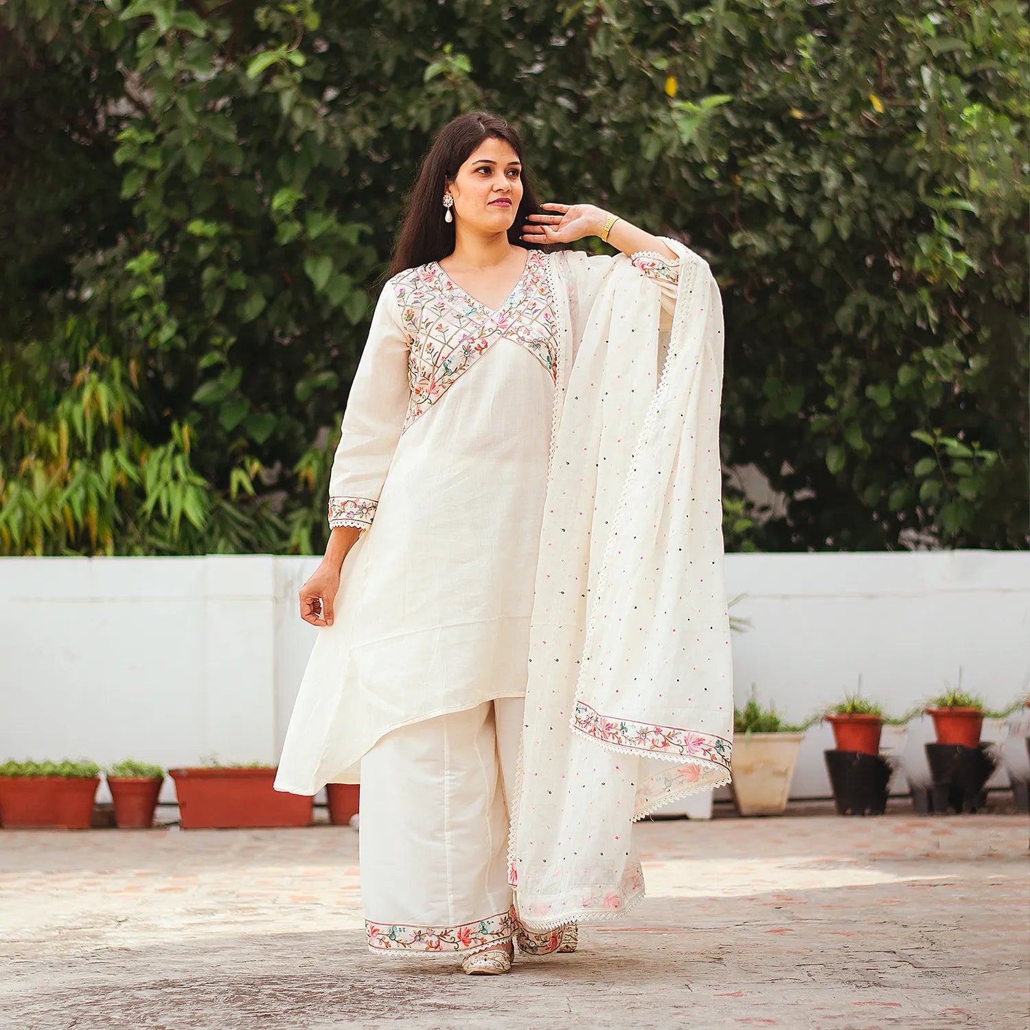 An Indian woman posing elegantly in a full-length off-white asymmetric kurta set