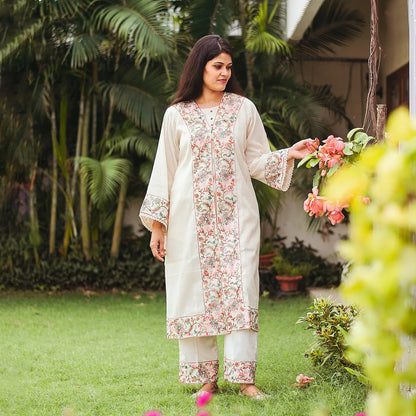 Indian model poses in an off-white cotton kurta and trousers with Kashmiri embroidery.