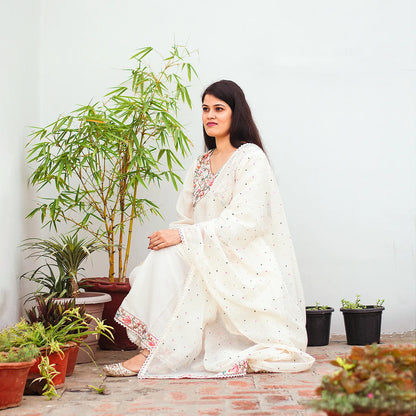 An Indian woman sitting gracefully, wearing an off-white asymmetric kurta set