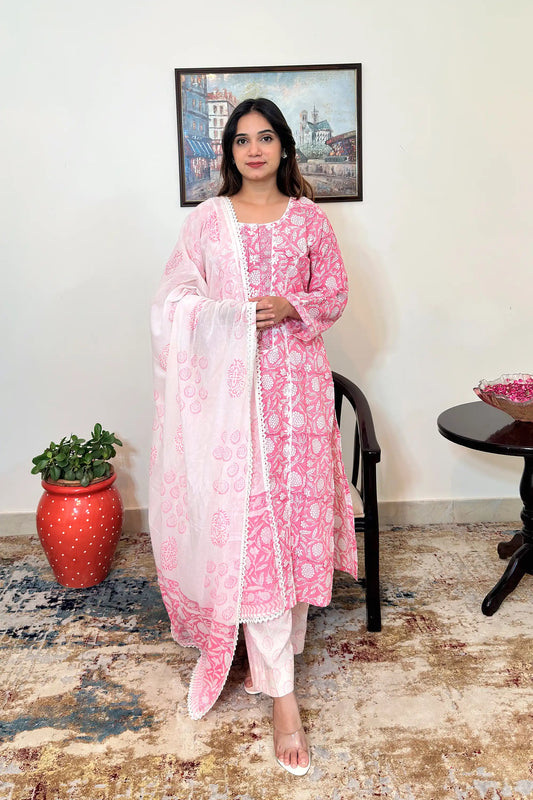 Front view of a model wearing a pink floral block-printed mulmul cotton kalidar kurta with an off-white appliqué yoke and appliqué work along the two front kalis, paired with off-white printed trousers and a white mulmul dupatta with pink floral block print and a lace-trimmed border.