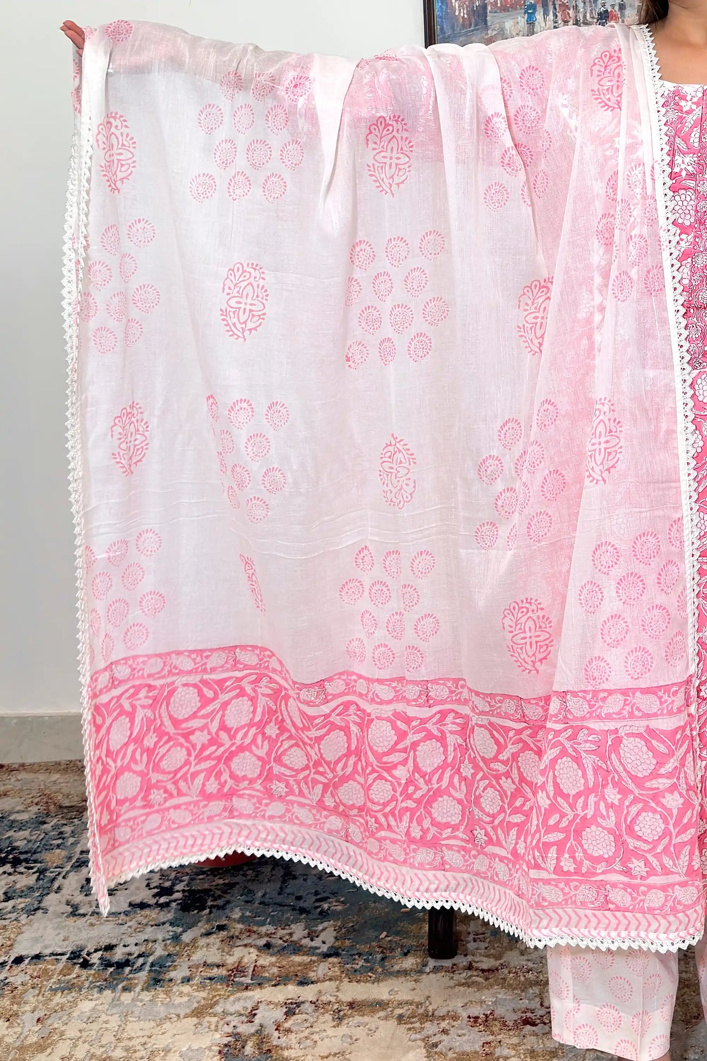 Close-up of the white mulmul dupatta held open, showing scattered pink floral and paisley block-print motifs and a lace-trimmed border along the edge.