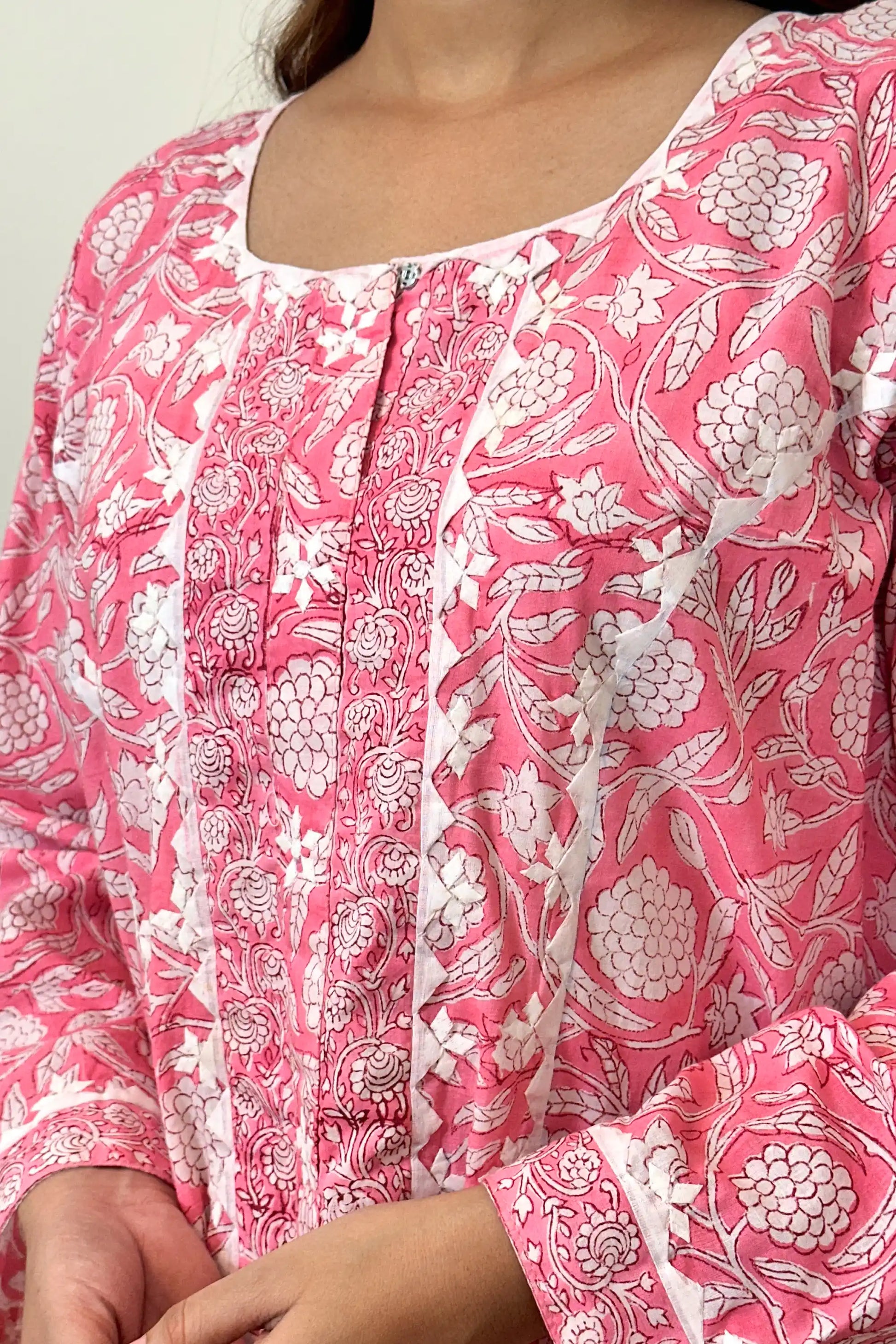 Close-up of the off-white appliqué yoke and neckline, showing the appliqué motifs, a metal hook-and-eye closure, and pink floral block print across the bodice.