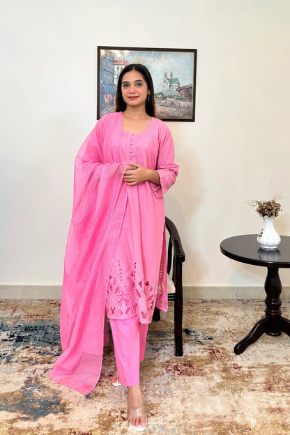 Front view of a model wearing a pink cotton straight kurta with a vertical line of small embroidered diamond and star motifs down the front panels and a floral cutwork hem, paired with pink trousers and a sheer pink supernet dupatta with scattered floral embroidery.