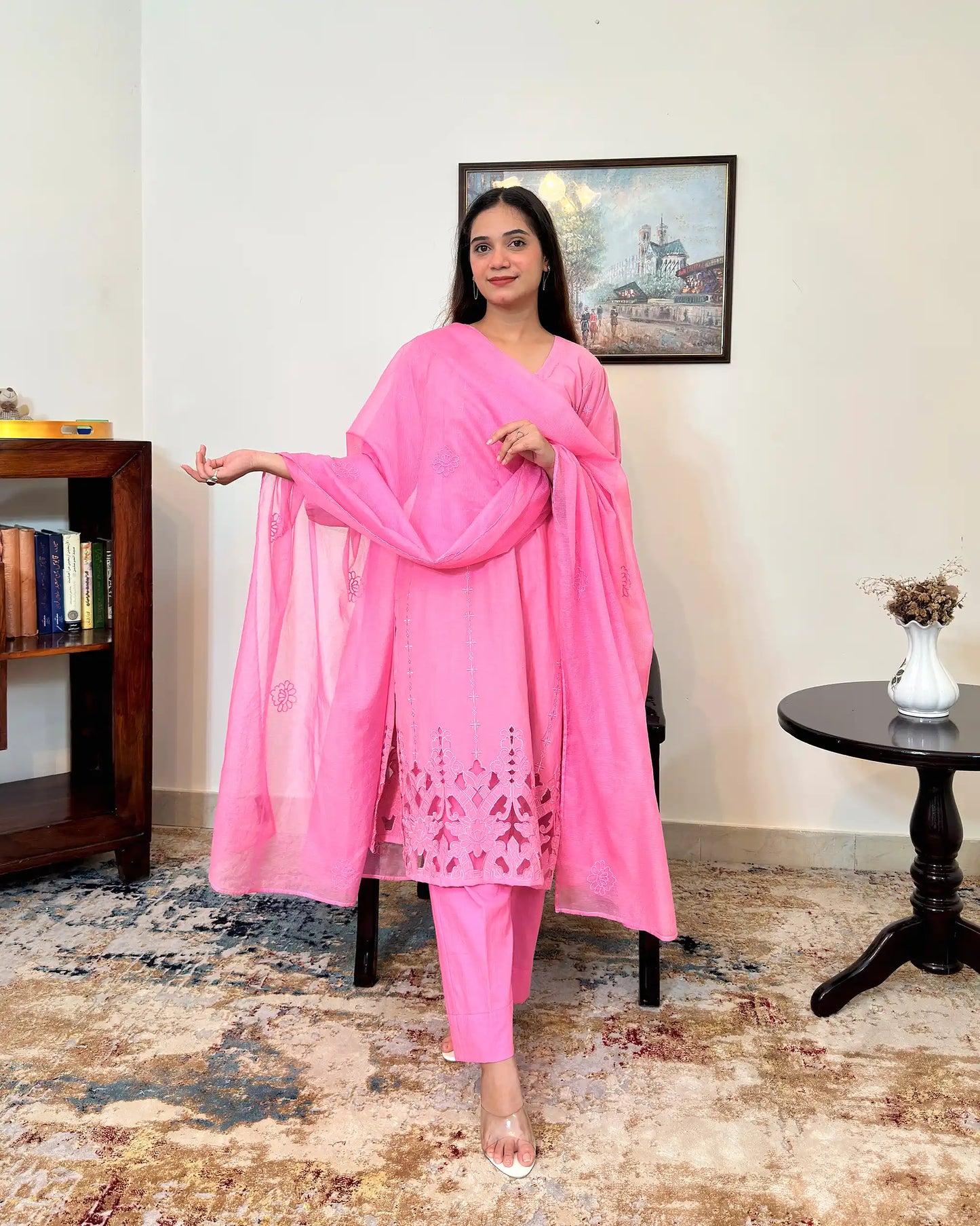 Model standing and holding the sheer pink supernet dupatta open with one arm extended, showing its scattered floral embroidery, with the kurta's floral cutwork hem visible.