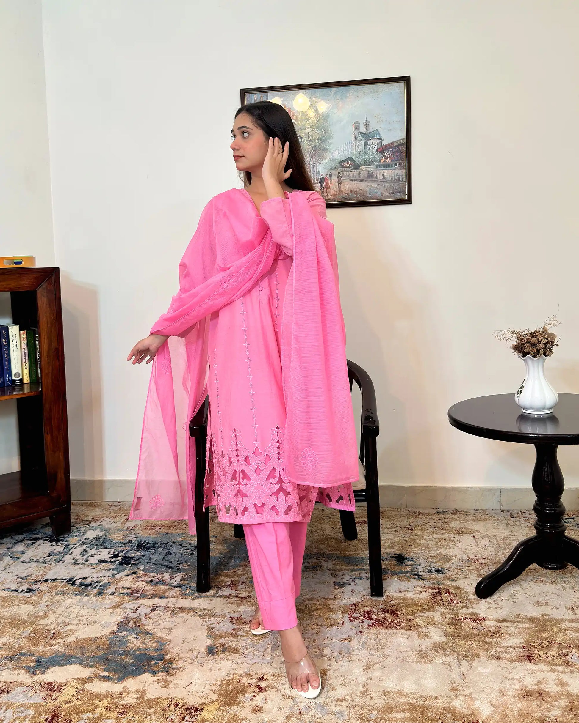 Model standing with one hand raised near the hair, looking to the side, wearing the pink cotton straight kurta with the sheer pink supernet dupatta and floral cutwork hem visible.