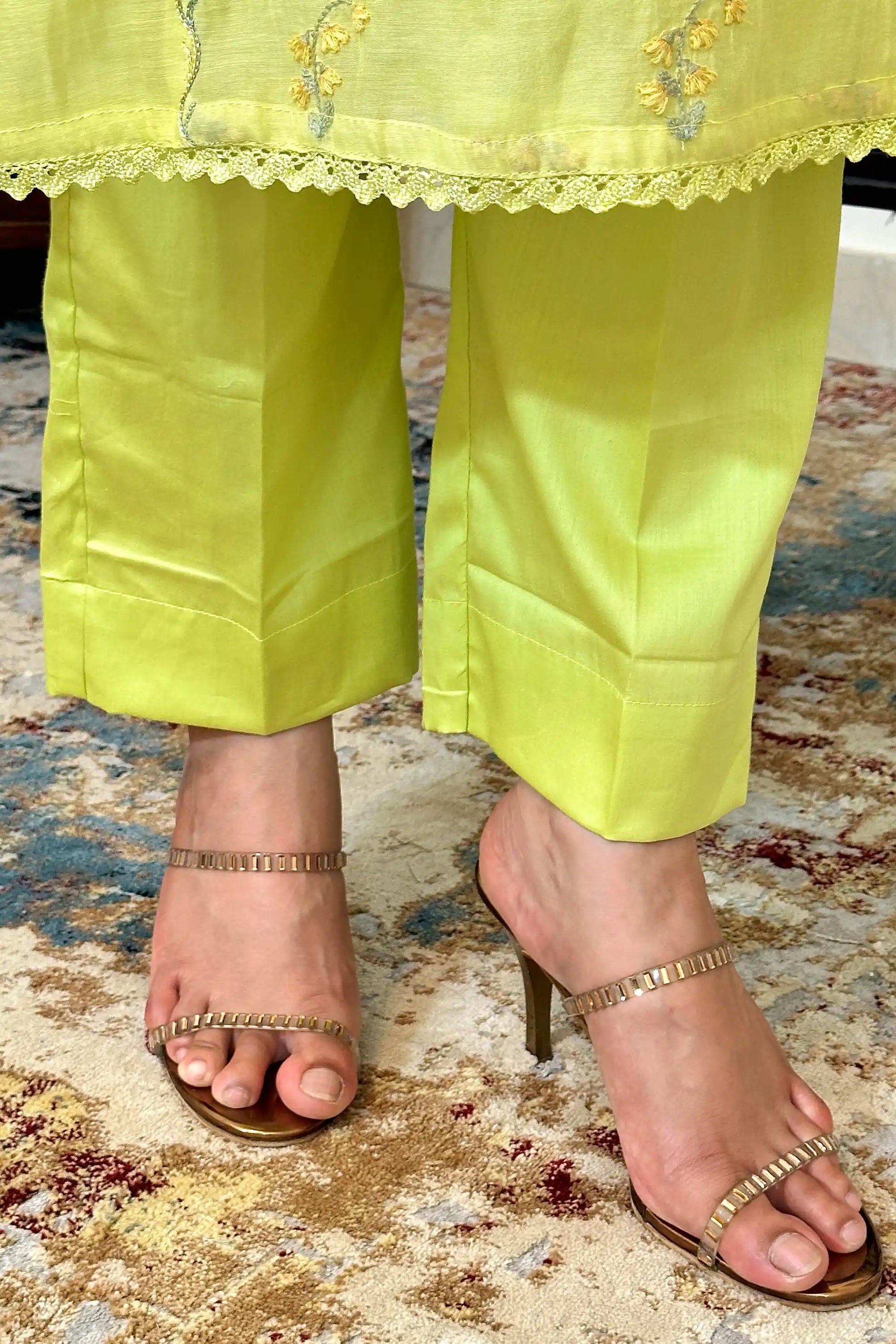 Close-up of the hem and trousers of a lemon-yellow chanderi kurta set, showing floral resham embroidery on the kurta hem with scalloped lace trim above lemon-yellow trousers.