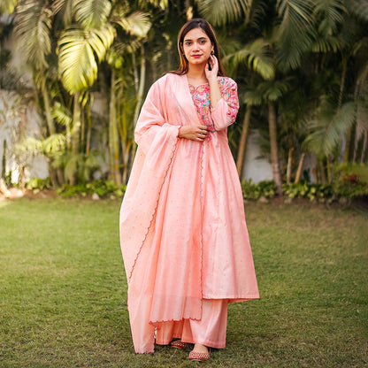  Indian lady posing in a peach Chanderi kurta set with floral resham embroidery and pink sequins.