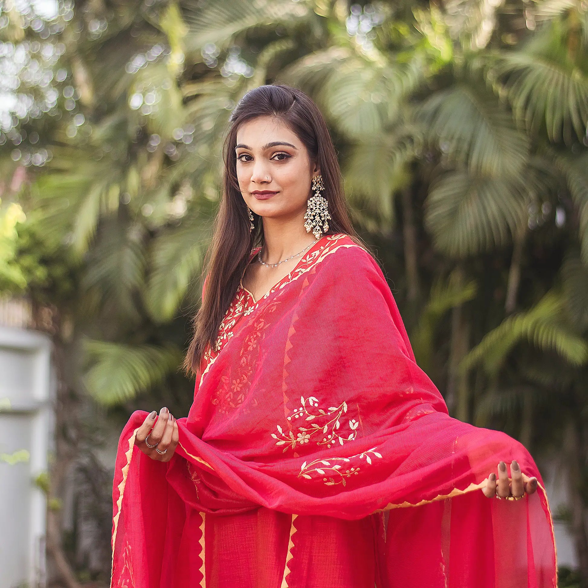 Close-up of an Indian model wearing a red jute silk kurta with beige applique work, holding the matching red chanderi dupatta.