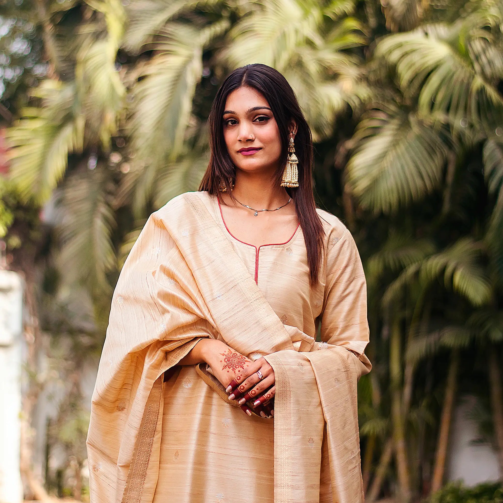 Close-up of an Indian model wearing a beige silk kurta with resham weave, holding a matching dupatta with banarasi motifs.