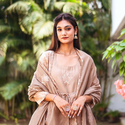 Upper half front view of a model wearing the beige floral print kurta set, featuring a beige floral print chanderi angrakha, matching palazzo, and a complementary beige chanderi dupatta.