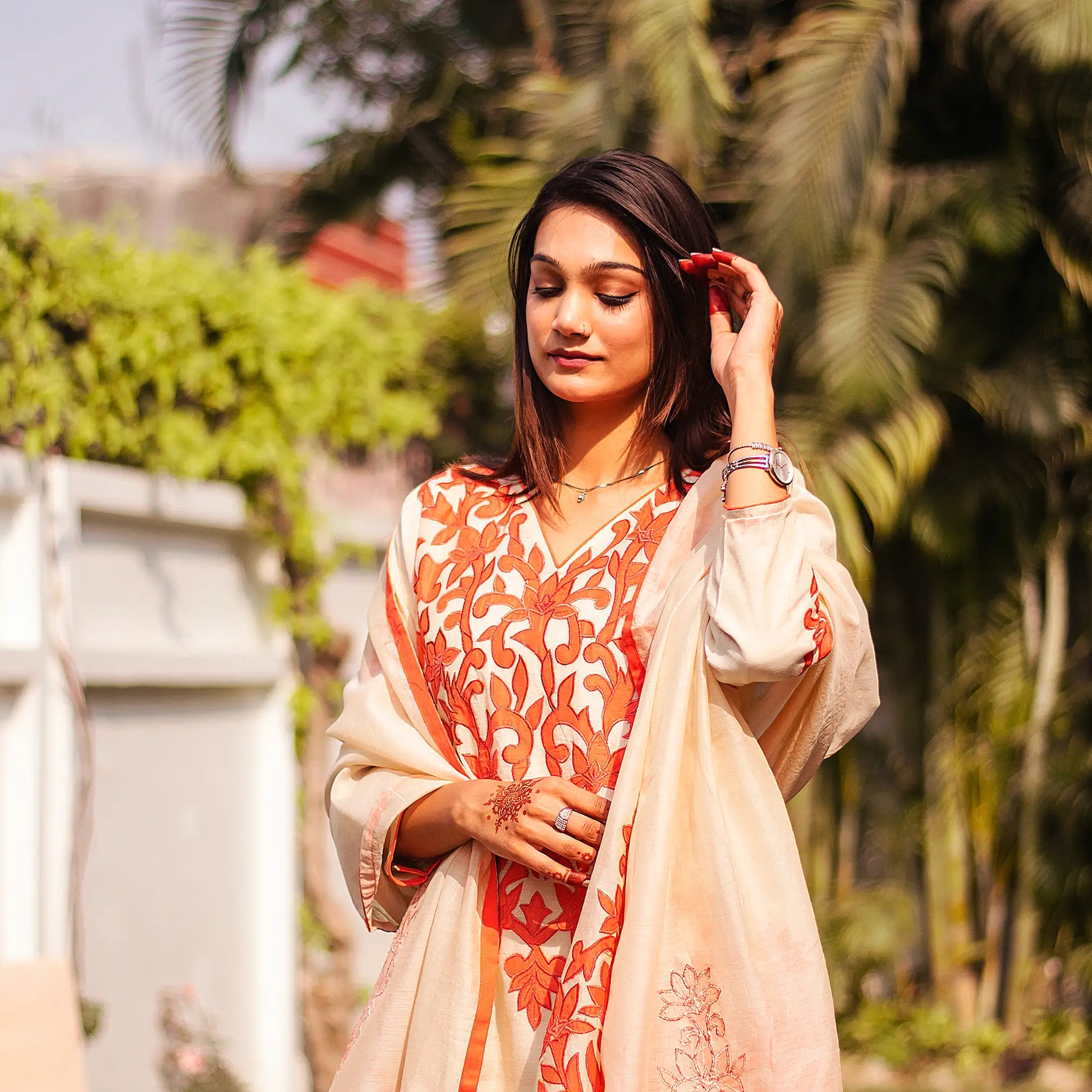 Close-up of an Indian model wearing a beige chanderi kurta with orange floral patchwork, holding a matching dupatta with patchwork paisleys.