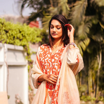 Close-up of an Indian model wearing a beige chanderi kurta with orange floral patchwork, holding a matching dupatta with patchwork paisleys.