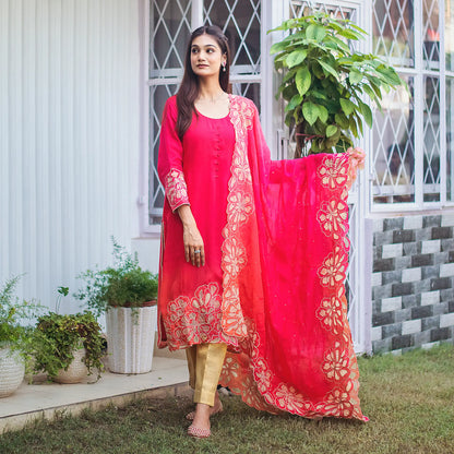 ndian model wearing a red organza kurta and dupatta with gold floral cutwork, paired with golden brocade trousers. 