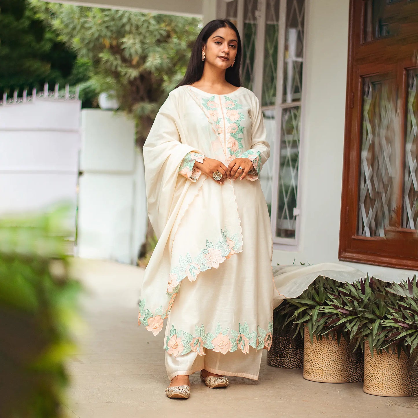 Indian woman wearing a cream chanderi kurta and dupatta with peach floral patchwork paired with cream palazzo.