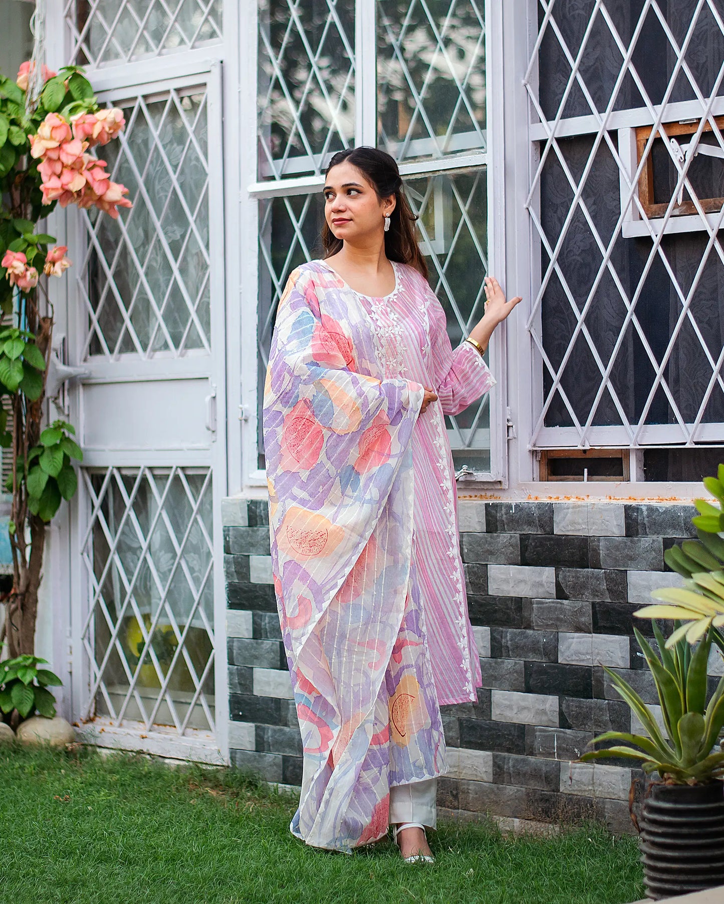 Model in a pink leheriya print kurta and matching pastel dupatta with kikri detailing and white trousers.