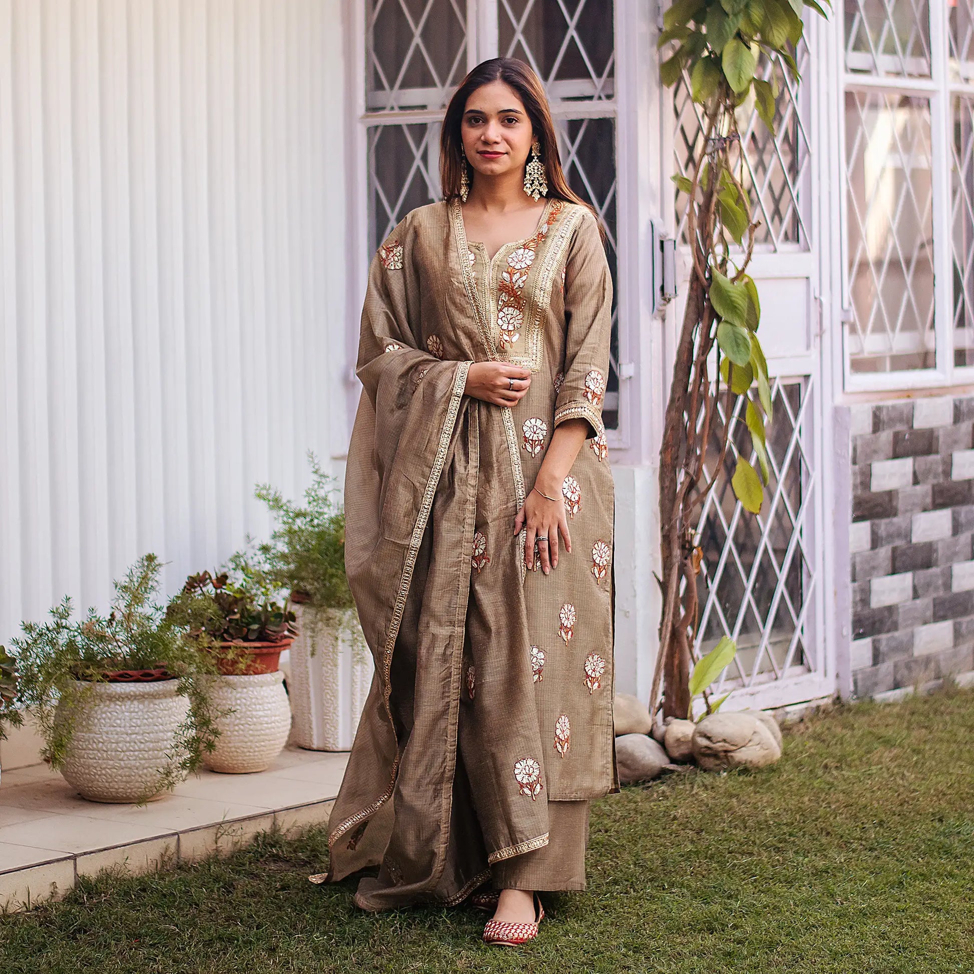 Indian model dressed in a beige Chanderi kurta and dupatta featuring golden gota patti embroidery, complemented by a beige palazzo.