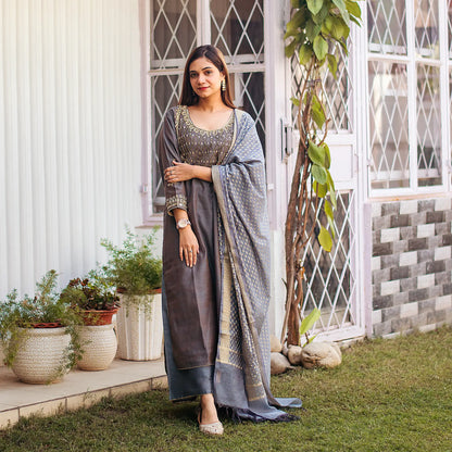 ndian woman wearing a grey silk kurta set, featuring golden zardozi embroidery, and accessorized with a grey banarasi dupatta and palazzo