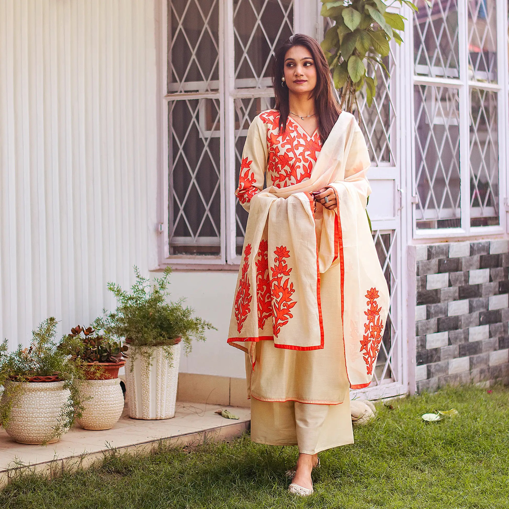 Indian model poses in a beige chanderi kurta and dupatta with orange floral patchwork and a beige palazzo.