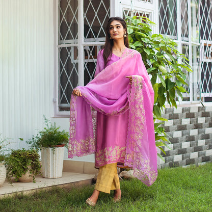 Indian model dressed in a light purple organza kurta that has  golden floral cutwork on both the kurta and dupatta, paired with gold trousers.