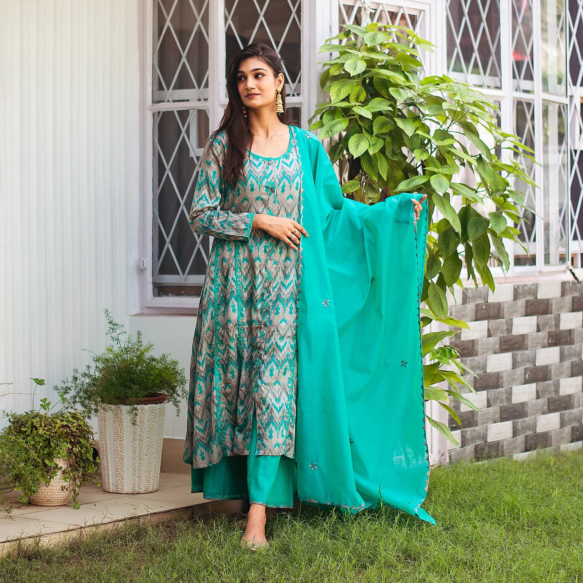 . Indian model in a green and grey ikat print kurta set with green applique work, holding a matching dupatta.