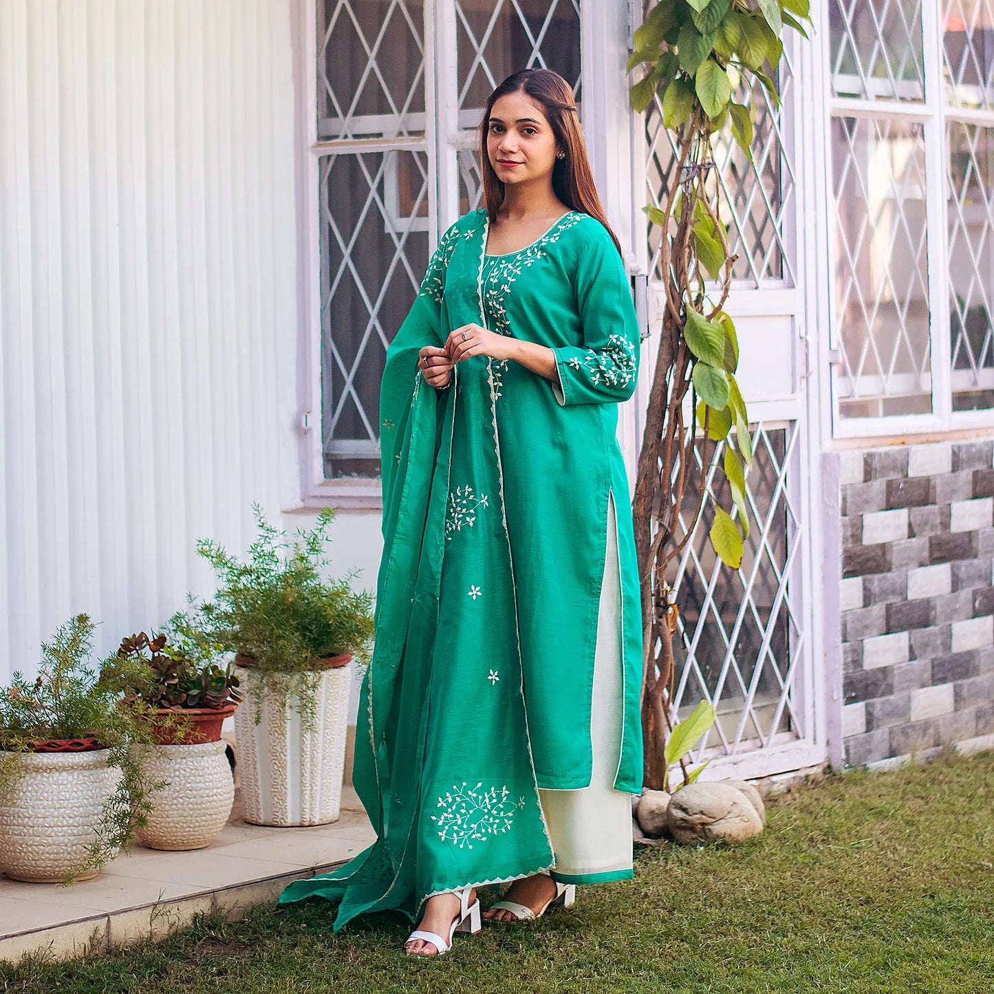 Full length pose of an indian model wearing green chanderi kurti and dupatta with applique work paired with white palazzo.