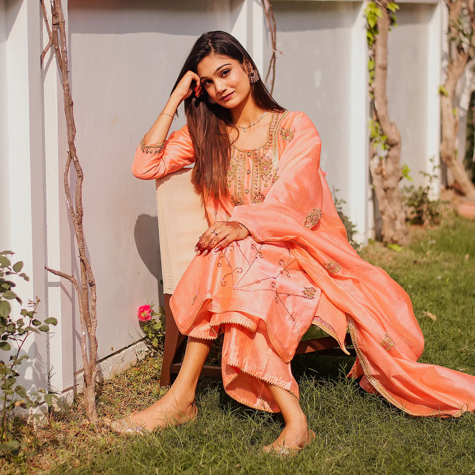 Woman in orange traditional outfit sitting on chair outdoors, smiling