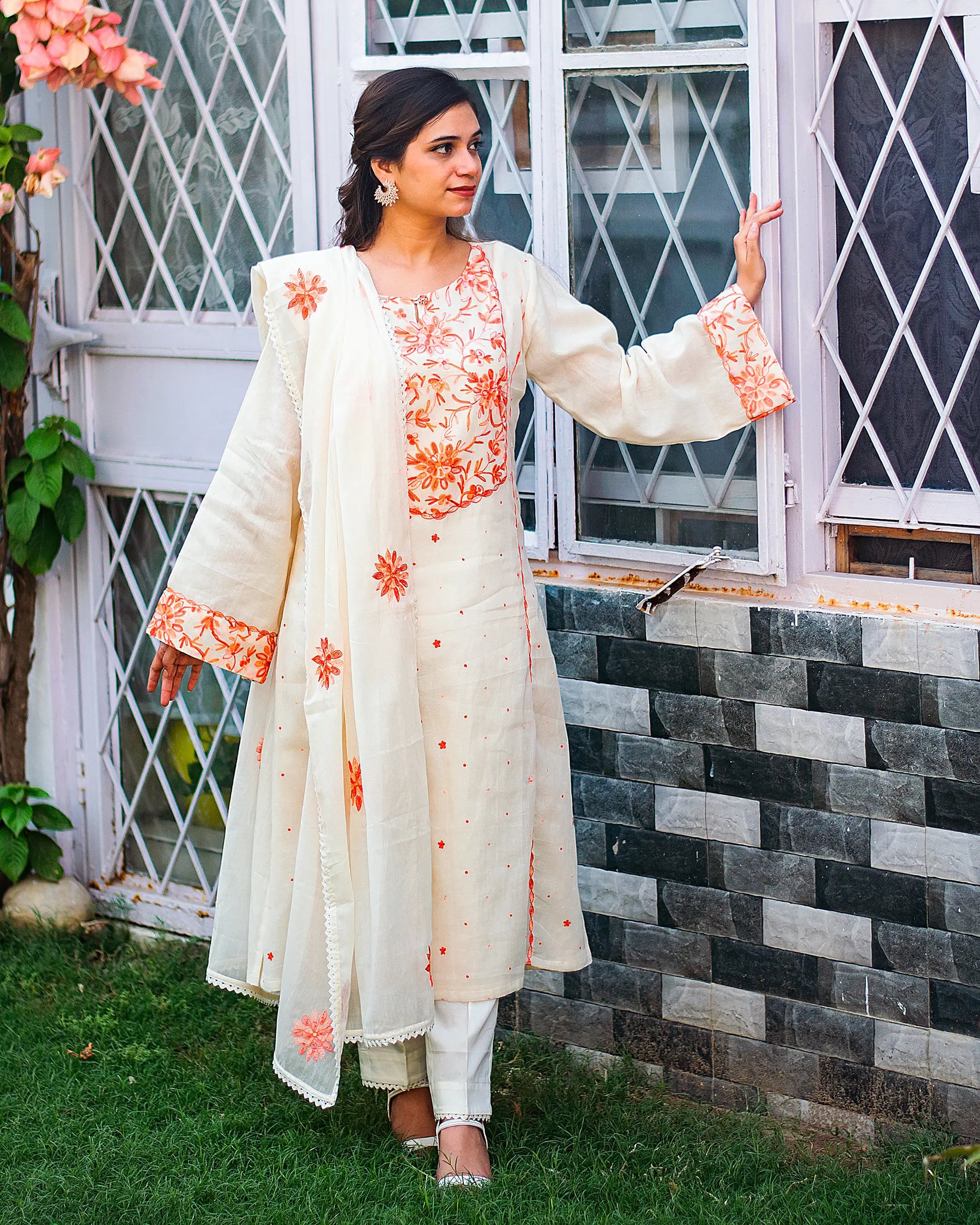 Indian model dressed in an off-white kurta adorned with peach Kashmiri embroidery, complemented by a matching dupatta and trousers.