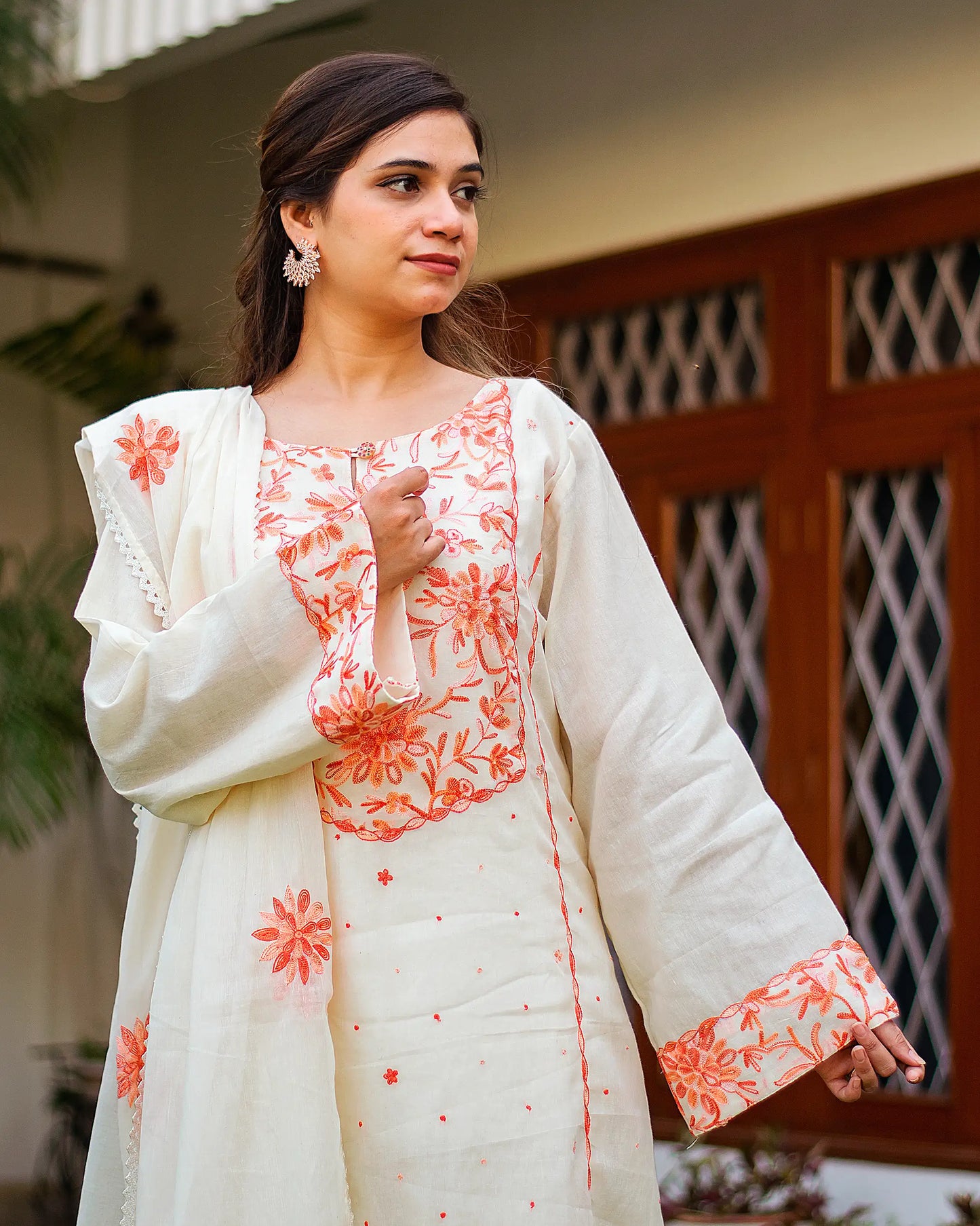 Close-up of an Indian model in an off-white kurta with peach Kashmiri embroidery and matching dupatta. 