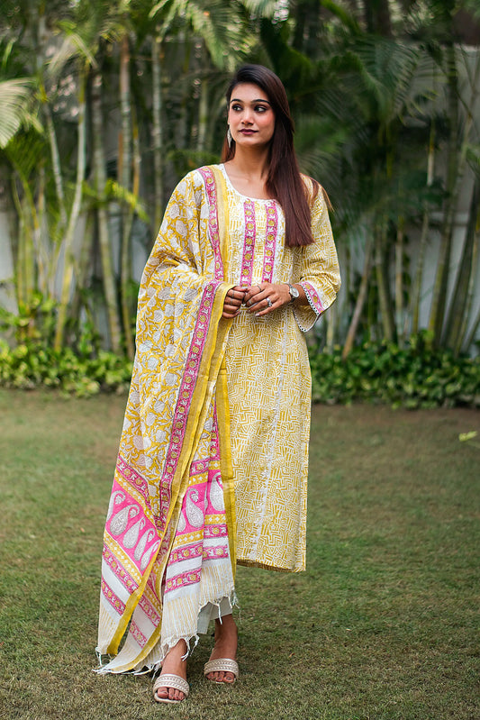 Front view (full suit, top to bottom): Model wearing a lemon yellow linen kurta with applique work, off-white trousers, and a printed dupatta.