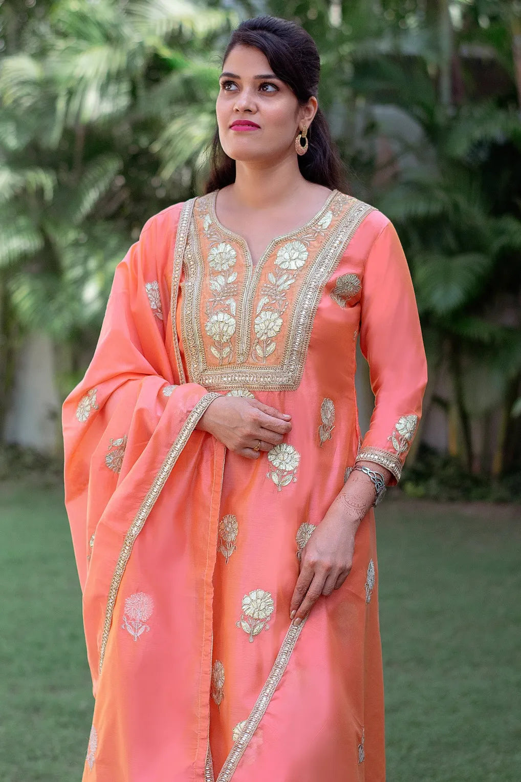 An Indian lady donning a Peach Chanderi Kurta with intricate Gota Work, paired with a matching Dupatta and a Golden Churidar.