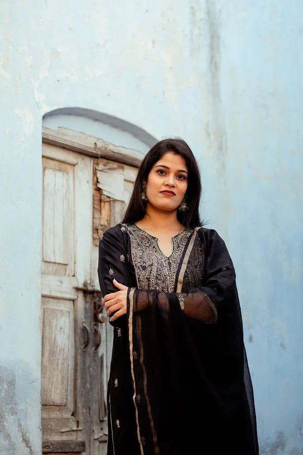 An elegant woman wearing a black silk kurta, black silk palazzo pants, and a black Chanderi dupatta with intricate work.