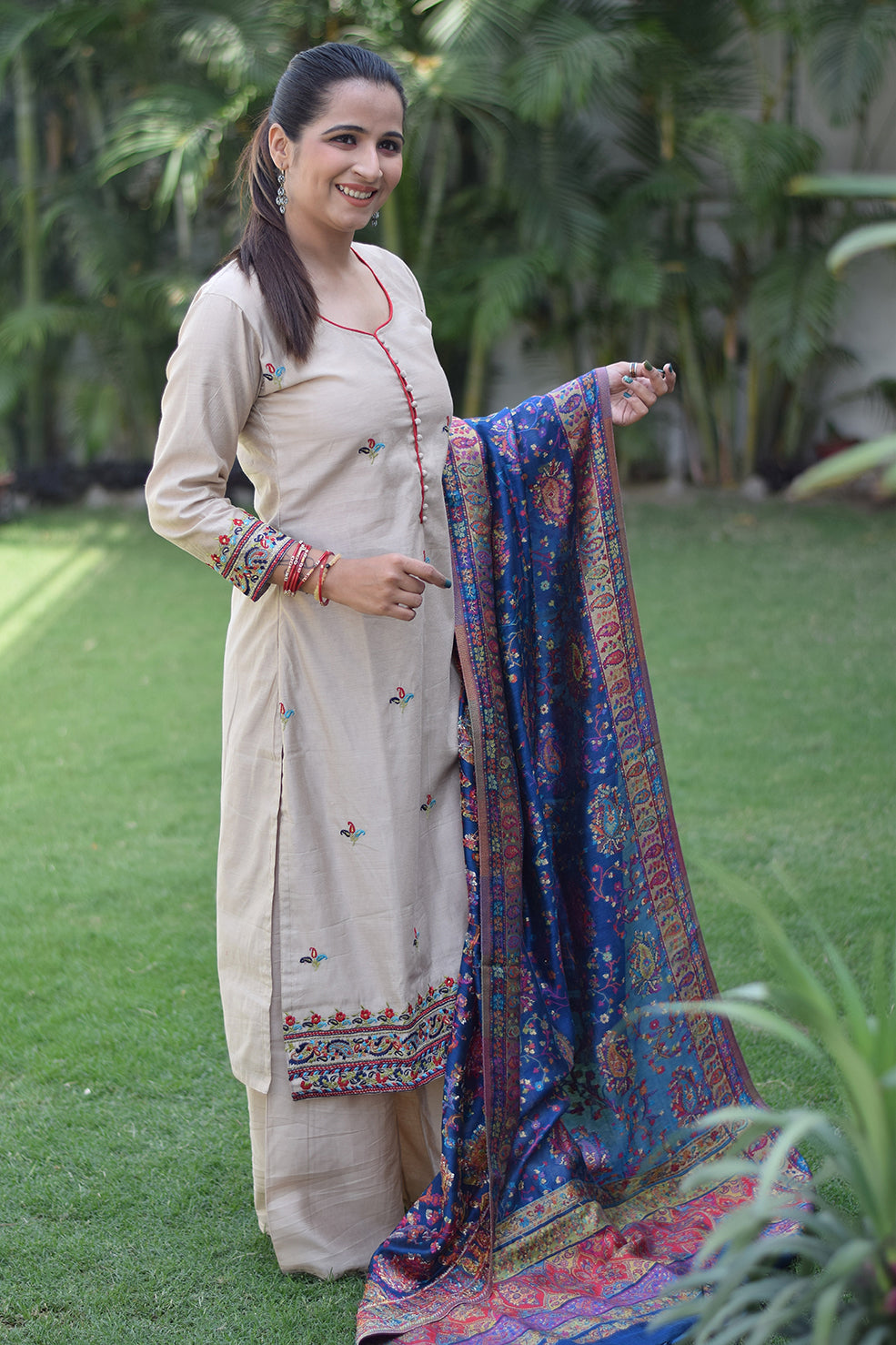 The beige kurta paired with a blue silk jamawar dupatta is worn by a woman standing alone.