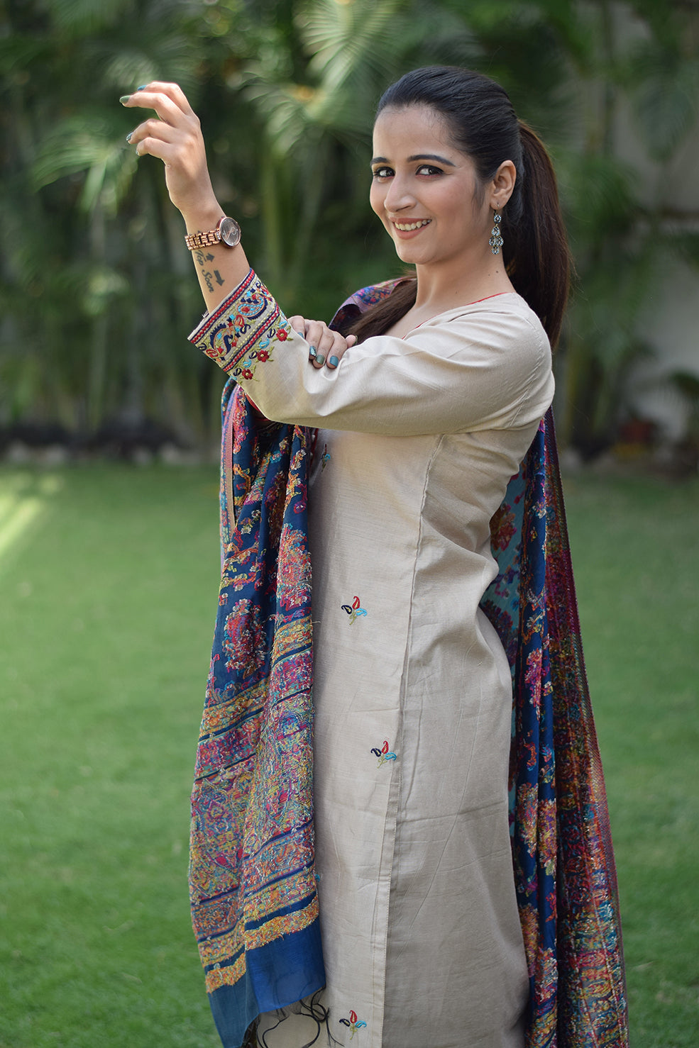 Solo female dons a beige kurta with a blue silk jamawar dupatta draped around her neck.