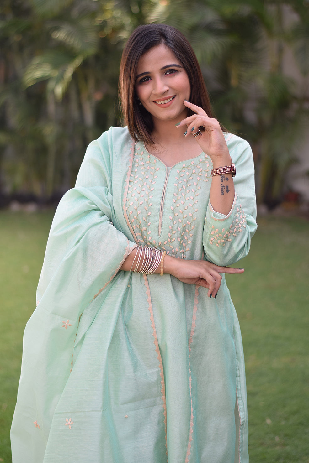A smiling Indian woman dressed in a sea green Aari work kurta