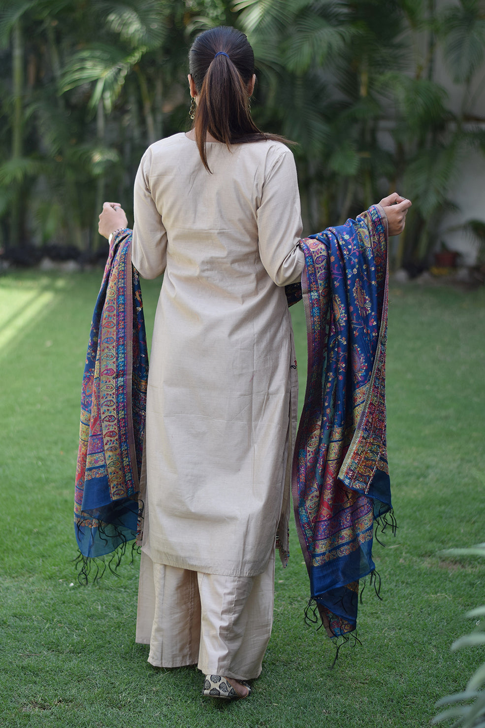 Woman wears a beige kurta with a blue silk jamawar dupatta, striking a confident pose.