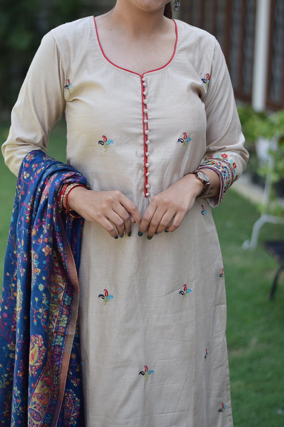 A woman standing solo models a beige kurta with a blue silk jamawar dupatta set.