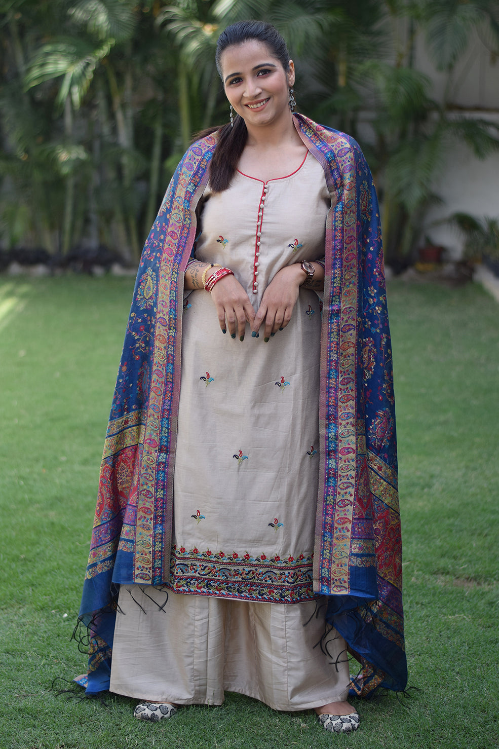 A woman is seen wearing a beige kurta with a blue silk jamawar dupatta draped over her shoulder.